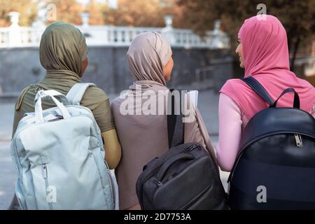 Three Muslim Ladies With Backpacks Walking Back To Camera Outdoor Stock Photo