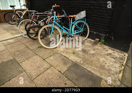 View of five leaning bicycles locked up on a pavement or sidewalk. Stock Photo