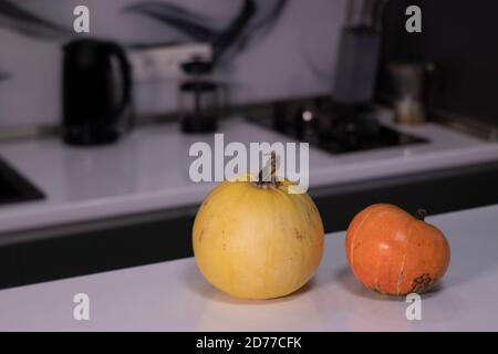 two pumpkins on white table in gray kitchen. halloween concept. Stock Photo