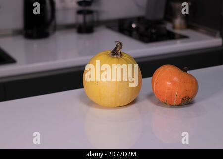 two pumpkins on white table in gray kitchen. halloween concept. Stock Photo