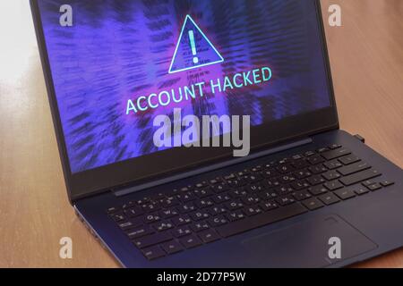 Laptop on the table and on a blue screen the text account is hacked. Warning triangular sign with exclamation mark symbol. Horizontal. Stock Photo