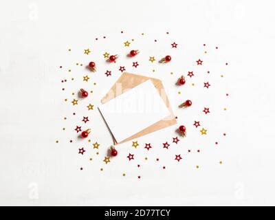 Empty card on craft envelope and various christmas decor on texture white background Holiday and invitation mockup. Top view. Stock Photo