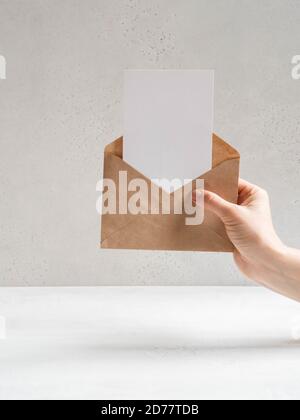 Female hand hold open kraft envelope and postcard on the grey background, front view. Copy space Stock Photo