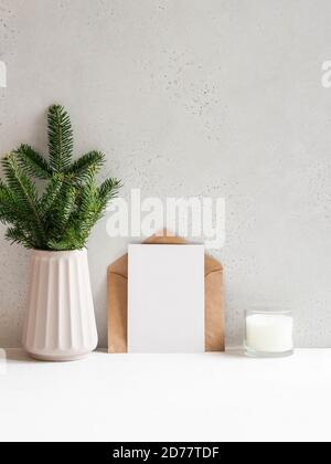 Christmas tree branches vase, open kraft envelope and empty postcard near the gray wall and glass candle. Front view. Copy space Stock Photo