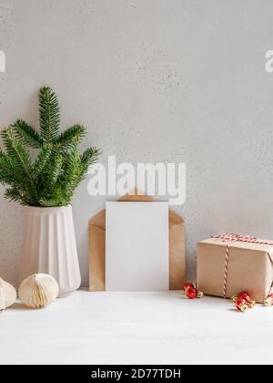 Christmas tree branches vase, open kraft envelope and empty postcard near the gray wall, wrapped gift and decor. Front view. Copy space Stock Photo