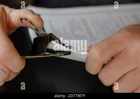 Close-up of male hands holding paper sheets with black metal clip. Sheets are filled with text. Traces of blue ink on man's finger. Selective focus. Stock Photo