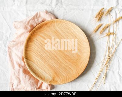 Round wooden craft tray and dry wheat ears on a white textile background. Top view. Copy space Stock Photo