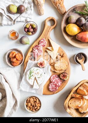 Snack set table. Variety of cheese, olives, sausage, baguette slices, figs, nuts on wooden board grey background, Flat lay. Top view. Stock Photo