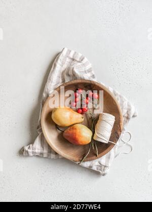 Autumn still life. Wooden bowl with pears and rose hips with red berries and a spool of thread on light background. Top view. copy space Stock Photo