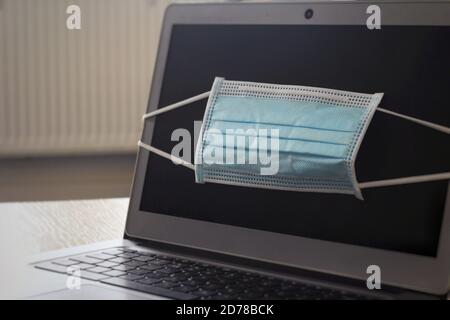 A laptop at home with a Coronavirus face mask over the screen. Studying from home and work from home concepts. Stock Photo