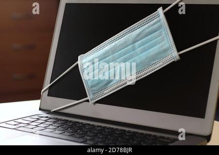 A laptop at home with a Coronavirus face mask over the screen. Studying from home and work from home concepts. Stock Photo
