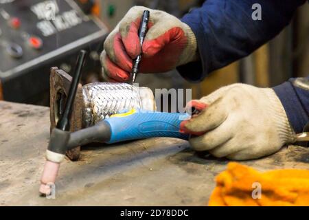 A worker marks the corrugation from the exhaust system of a passenger car with a marker in white protective gloves Stock Photo
