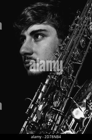 Grayscale shot of a handsome guy holding his saxophone on a dark background Stock Photo