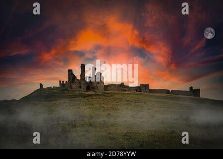 Dawn over Dunstanburgh Castle on the Northumbrian coast. Stock Photo