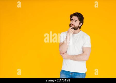 Close up portrait of thoughtful man who looks away touching his chin and weighs the pluses and minuses . offer isolated on bright yellow background Stock Photo