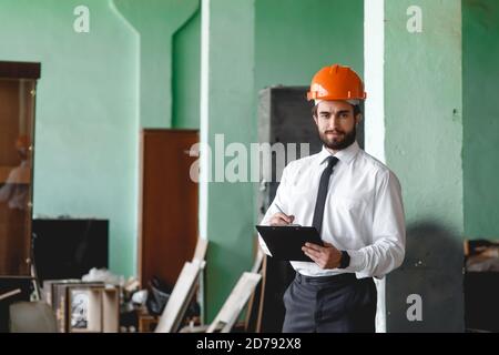 A young bearded Architect in a construction helmet on a construction site checks the result Stock Photo