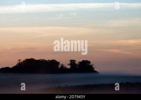 The Sun begins to rise above the Wiltshire landscape during the Summer Solstice at Stonehenge. Stock Photo