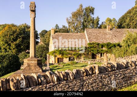 Evening light on the war memorial in St Barnabas churchyard and a traditional stone cottage in the Cotswold village of Snowshill, Gloucestershire UK Stock Photo