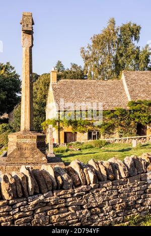 Evening light on the war memorial in St Barnabas churchyard and a traditional stone cottage in the Cotswold village of Snowshill, Gloucestershire UK Stock Photo