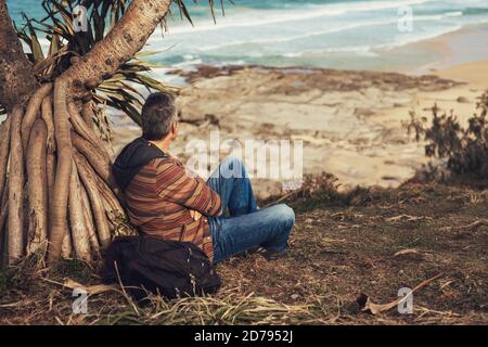Middle-aged man sitting under the tree at the ocean. Stock Photo