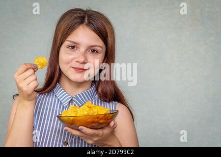 A young girl holds a plate with chips in her hand, chips in the other, smiles and is ready to eat this fast food. Selective focus Stock Photo