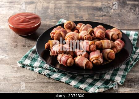 Pig in blankets. Sausages wrapped in smoked bacon on wooden table Stock Photo