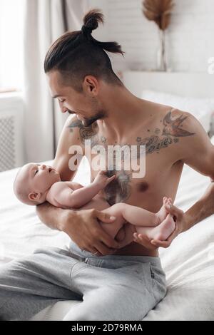 man with infant. happy family at home. happy father with cute two months baby boy laying in light bed at home Stock Photo