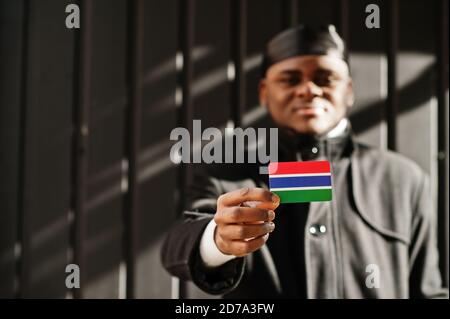 African man wear black durag hold Gambia flag at hand isolated dark background. Stock Photo