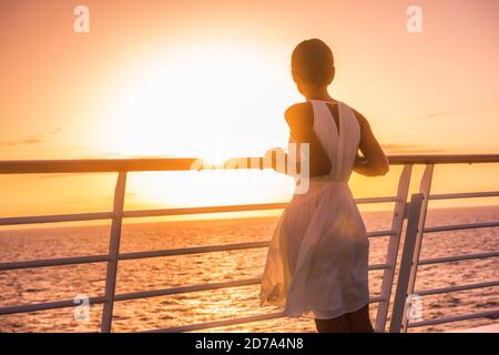 Cruise ship vacation woman travel watching sunset at sea ocean view. Elegant lady in white dress relaxing on deck balcony, luxury holiday destination. Stock Photo