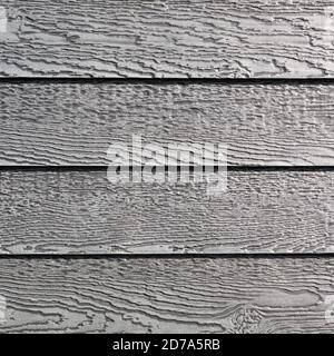 Several rows of gray vinyl siding with imitation wood grain the in the early morning light. Stock Photo