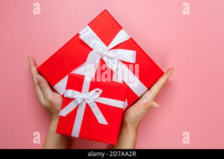 Flat lay of woman hands holding gift wrapped and decorated with bow isolated on pink background with copy space. Valentines love. Birthday theme. Stock Photo