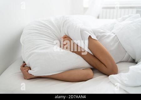 Depressed woman lying alone on bed covering head with pillow feeling afraid or depressed suffer from insomnia, loud sounds of neighbors, has mental pr Stock Photo