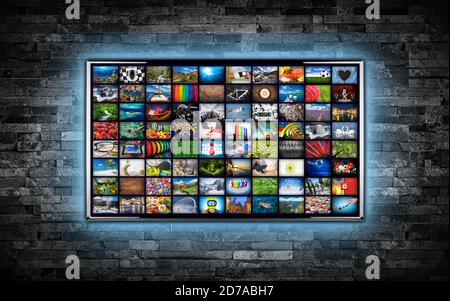 black flat tv screen display with picture movie gallery backdrop. television wall mounted on dark slate stone wall glowing blue LED background. Multim Stock Photo