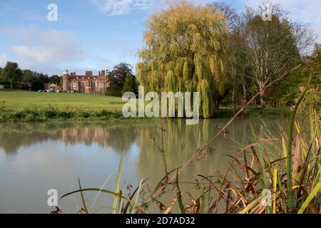 Parkland setting of river and willow tree in front of mansion of Madingley Hall, Near Cambridge Stock Photo