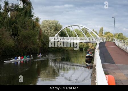 White riverside bridge for walking and cycling. Riverside Bridge on River Cam in Cambridge showing rowers and Canal boats moored Stock Photo