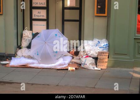 Man sleeping rough in doorway of empty commercial building with a Microsoft umbrella empty MacDonald container and various plastic bags Stock Photo
