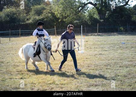 Woman leading small grey pony and determined young boy rider at local riding gymkhana competition England Stock Photo