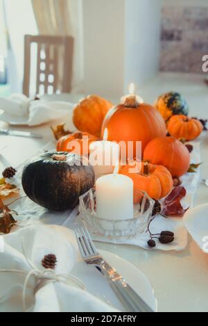 Festive table setting for Thanksgiving family home dinner. Fall composition with decorative pumpkins, nuts, cones, fallen leaves, and candles in light Stock Photo