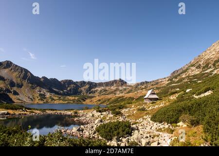 Five Polish Ponds Valley landscape in High Tatra Mountains with Czarny Staw Polski Lake and small wooden mountain hut on a glade, Poland. Stock Photo