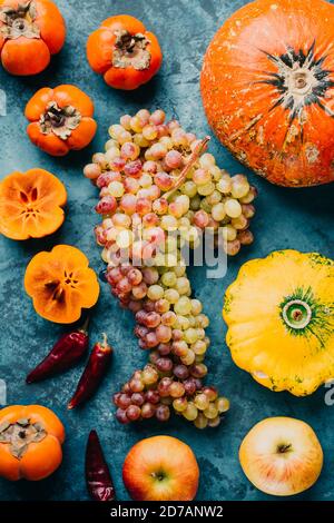 Autumnal fruits and vegetables. A bunch of grapes, pumpkin and persimmon on a blue background. Stock Photo