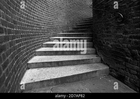 Black and white monochrome image of looking up some winding street steps curving to the right in an alleyway. Stock Photo