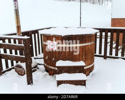 Wooden furaco baptismal font strewn with snow stands on a terrace with a wooden fence on a snowy winter day Stock Photo