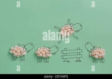 Counting sheep made of cotton balls jumping over the fence. Creative concept of mixing real objects and computer graphic. Stock Photo