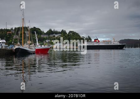 Boats moored in Oban harbor and a ferry leaving the harbor on a cloudy day, Scotland Stock Photo