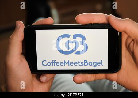 Coffee meets bagel logo on the screen of mobile phone in mans hand. Application for dating and acquaintance. Man is laying on the sofa and looking for Stock Photo