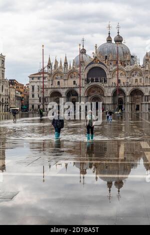High water - Acqua Alta causing flooding in Piazza San Marco. Tourists wading through water in wellingtons. St Marks Basilica St Marks Square, Venice Stock Photo