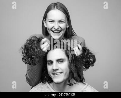 Funny time together. Joyful moments in pairs. Cheerful girl holding curly hair of boyfriend makes him funny hairstyles. Stock Photo