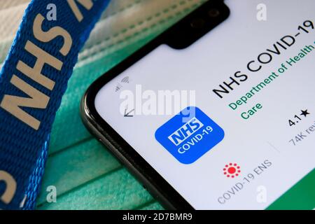 NHS COVID-19 app seen in Play Store on the screen of smartphone next to viral masks and NHS lanyard. Stock Photo