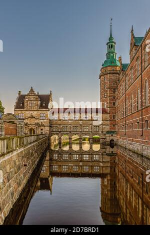 Frederiksborg castle and bridge over the moat are reflected in the shiny water an early morning at sunrise, Hillerod, Denmark, October 17, 2020
