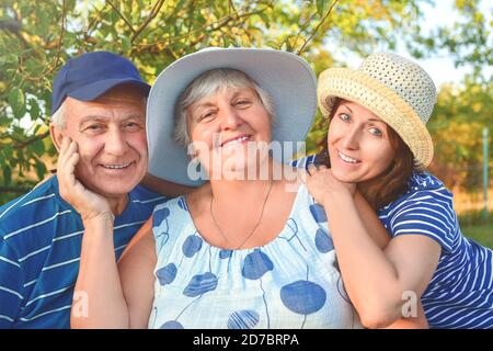 Beautiful senior couple is sitting on the bench in the park with their adult daughter. Grandma and grandpa are hugging and smiling. Real love and fami Stock Photo